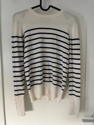 Ljus beige och marinblå randig tröja - Klassisk långärmad tröja i ljus beige med marinblå horisontella ränder.Den har  även guldiga knappar vid ärmen Den är ifrån Zara och är i storlek S Nästan aldrig använd!