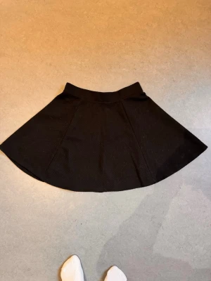 Svart kjol med struktur - Fin kjol med struktur. Går ned till strax ovanför knäet på mig som är 160 cm lång. Inte mycket använd. Har lite katthår på sig.