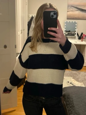 Randig stickad tröja i blått och vitt - Säljer en stickad tröja med breda marinblå och vita ränder. Tröjan har en avslappnad passform, rund halsringning och långa ärmar. Perfekt för dig som gillar en enkel men snygg stil. Materialet soppar till en mysig känsla. Säljer då den tyvärr ej kommer till användning längre då jag har många liknande tröjor💕