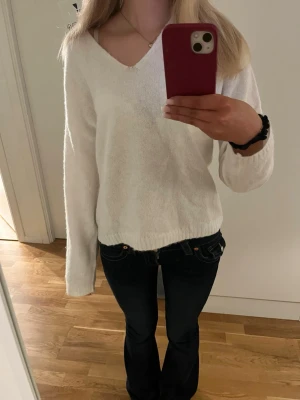 Vit stickad tröja med v-ringning - Säljer en enkel och stilren vit stickad tröja med v-ringad hals. Tröjan har långa ärmar och ribbade muddar vid ärmslut och nederkant. Perfekt att matcha med jeans för en avslappnad look.