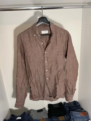 Brun linneskjorta från John Henric - Säljer en brun skjorta från John Henric i 100% linne med klassisk krage och vita knappar. Skjortan har lång ärm och en avslappnad passform. Hör gärna av dig vid frågor!