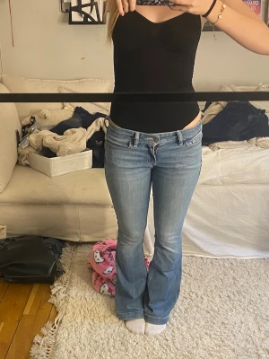 Ljusblå bootcut jeans - Säljer ett par ljusblå bootcut jeans med klassisk femficksdesign och låg midja. Jeansen har en snygg tvätt och sitter tajt över låren för att sedan bli vidare nedtill. Från hollsister och är i bra skick.