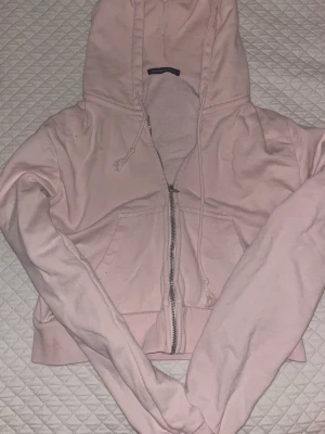 Ljusrosa hoodie från Brandy Melville - Söt ljusrosa hoodie från Brandy Melville med dragkedja framtill, huva med dragsko och två fickor. Köpt från Sellpy, väldigt stel i formen och har ett hål på baksidan