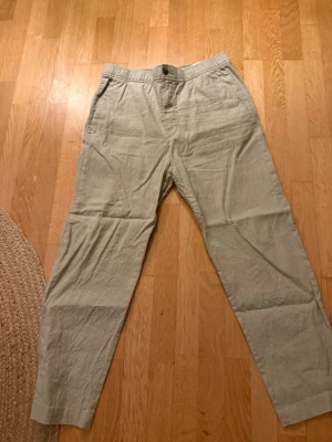 Beige linnebyxor från H&M - Säljer ett par beige linnebyxor från H&M med avslappnad passform och resår i midjan. Byxorna har raka ben och sidofickor, perfekta för en chill och stilren look. Materialet är 100% linne vilket gör dem svala och sköna.
