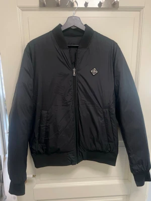 Svart pufferjacka från j.lindberg - Säljer en svart pufferjacka från J.lindberg som har två sidor. Jackan har två sidofickor, dragkedja framtill och en liten logotyp på bröstet. Klassisk quiltad design som håller dig varm under kalla dagar.