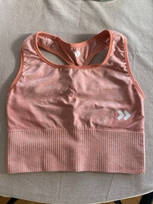 Rosa sport-bh - Säljer en snygg rosa sport-bh från Lager 157 med ribbad nederkant och brottarrygg. Materialet är stretchigt och andas, perfekt för träning. Logga framtill och coolt kors i ryggen för extra stöd och stil. Aldrig använd!