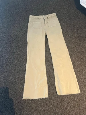 Gröna/kakhi utsvängda jeans - Snygga jeans med utsvängda ben och rå kant nedtill. Byxorna har klassiska fickor både fram och bak. Solen gjorde så att byxorna såg mer beiga ut än vad de är!
