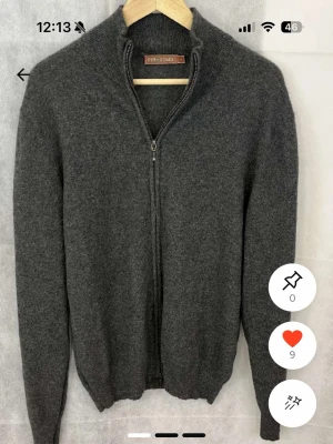 Mörkgrå ziptröja från Per Uomo - Mörkgrå ziptröja från Per Uomo i mjukt stickat material. Tröjan har hög krage, hel dragkedja framtill och ribbade muddar vid ärmslut och nederkant. Perfekt för lager på lager och enkel att matcha med olika outfits.