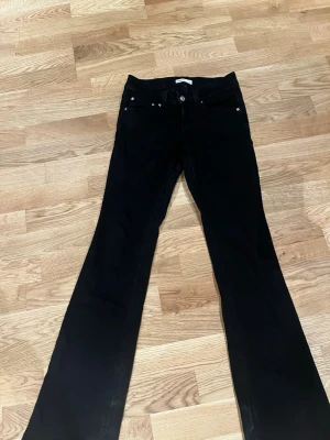 Svarta bootcut jeans från Gina tricot med silverknappar  - Snygga svarta bootcut jeans med klassisk femficksdesign och silverfärgade knappar. Jeansen har utsvängda ben och normal midja, perfekta för en trendig och avslappnad stil. Dem är lite andvända med inte slitna.