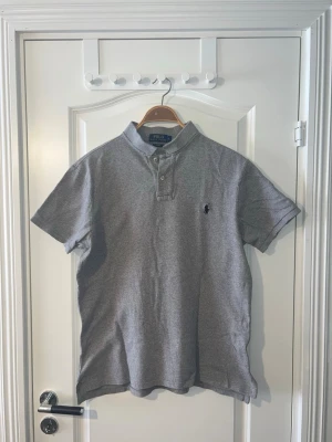 Grå kortärmad skjorta Polo Ralph Lauren - Polo Ralph Lauren piké i grå färg, storlek L (Slim Fit). Tröjan är i mycket bra skick och har bara använts ett fåtal gånger. Klassisk och stilren piké som passar bra både till vardag och lite mer uppklädda tillfällen. Finns att hämta i Södertälje eller Örebro.