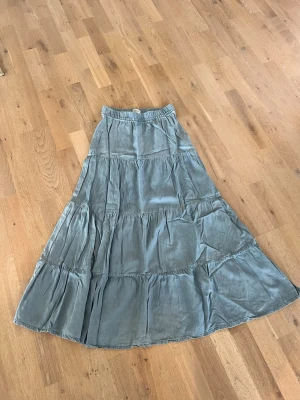 Ljusblå långkjol från ONLY - Luftig och flowy ljusblå långkjol i lätt jeans-tyg, från ONLY med resår i midjan. Kjolen har flera volanger och är tillverkad i ett mjukt och lätt material som passar perfekt till varmare dagar.