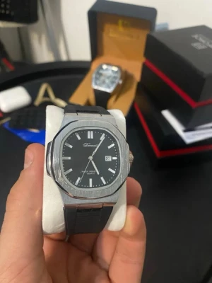 Svart herrklocka från Burei - Stilren herrklocka från Burei med svart urtavla, silverfärgat åttakantigt boett och svart armband. Klockan har tydliga vita index, datumvisning och quartz-urverk. Perfekt accessoar för dig som gillar en klassisk och modern look.