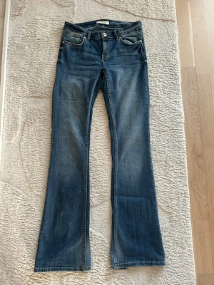 Blå bootcut jeans  - Snygga blå bootcut jeans med klassisk femficksdesign och lätt slitning. Jeansen har normal midja och är tillverkade i mjuk denim med lite stretch för extra komfort. Perfekta för en avslappnad och trendig look.