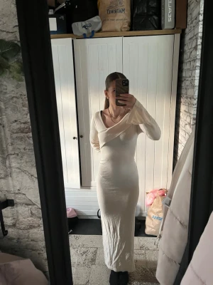 Lång beige omlottklänning - Elegant långklänning i beige färg med omlott-detalj och v-ringad hals. Klänningen har långärmade ärmar och en figurnära passform som framhäver siluetten. Perfekt för dig som vill ha en stilren och modern look.