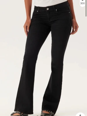 Svarta bootcut jeans - Snygga svarta bootcut jeans med klassisk femficksdesign och normal midja. Jeansen har en lätt utsvängd passform nedtill och stängs med knapp och dragkedja. Perfekta till sneakers eller boots för en trendig look. Helt nya byxor som aldrig använts 