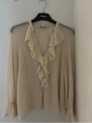 Beige volangblus från Zara - Söt beige blus från Zara med volangdetaljer längs ringningen och framtill. 