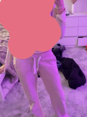 Ljusrosa mjukisbyxor från russemerch - Säljer ett par ljusrosa mjukisbyxor med dragsko i midjan och resår vid bensluten. Byxorna har en relaxed fit och är perfekta för chill dagar. Tillverkade i mjukt material som känns skönt mot huden. Passar dig som gillar en avslappnad stil.