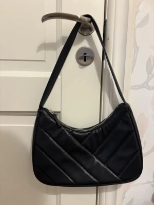 Svart axelväska - Super snygg svart handväska med axelrem och silverfärgad dragkedja. Väskan har en mjuk, rundad form och är tillverkad i konstläder. Insidan är fodrad i svart tyg och har en liten innerficka. Perfekt för dig som gillar stilrena accessoarer. Skriv gärna innan ni köper❤️