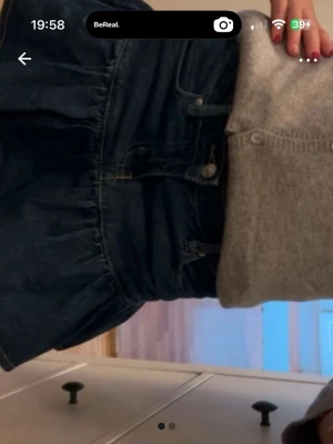 Mörkblå jeanskjol med låg midja - Säljer en mörkblå jeanskjol med låg midja och volangkant. Kjolen har knappar och fickor framtill, samt en klassisk denimlook. Perfekt att styla med en stickad tröja eller t-shirt för en trendig vardagsoutfit. 