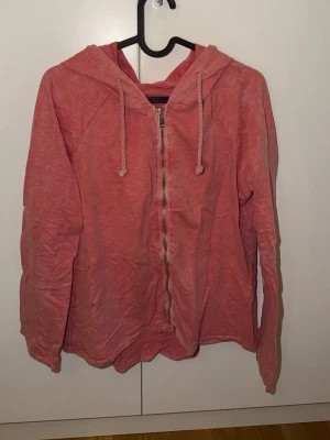 Rosa zip-hoodie med dragsko - En chill rosa hoodie med dragkedja framtill och huva med dragsko. Tillverkad i mjukt och lätt material, perfekt för lager-på-lager. Långa ärmar och enkel design utan tryck eller logga.