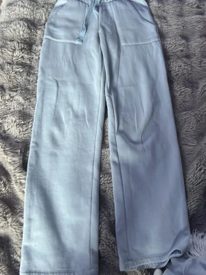 Ljusblåa vida mjukisbyxor - Säljer ett par ljusblå mjukisbyxor med breda ben och dragsko i midjan. Byxorna har två fickor framtill och är gjorda i ett mjukt, bekvämt material som känns skönt mot huden. Perfekta för chill dagar eller när du vill vara extra comfy.