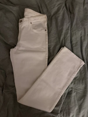Vita raka jeans från Lee - Säljer ett par vita jeans från Lee med raka ben. Jeansen har metallknapp med Lee-logga.