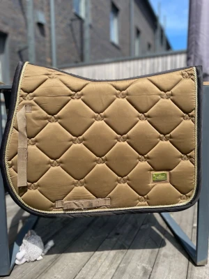 Brunt schabrak från Equestrian Stockholm - Säljer ett snyggt brunt schabrak från Equestrian Stockholm. Schabraket har svarta kanter och kardborrefästen. 