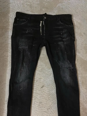 Dsquared2 jeans - Säljer ett par svarta skinny jeans från Represent med slitningar och distressed detaljer på benen. Jeansen har dragkedja i gylfen, fem fickor och coola färgstänk för en edgy look. Perfekta för dig som gillar streetwear och vill sticka ut.