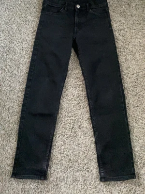Svarta raka jeans - Säljer ett par svarta jeans med rak passform och klassisk femficksdesign. Jeansen har knapp och dragkedja framtill samt bälteshällor i midjan. Perfekta till en avslappnad och stilren look.