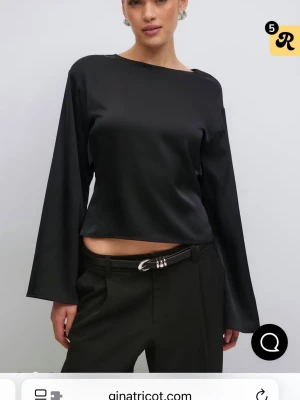 Svart satinblus med öppen rygg - Trendig svart topp i satin från Gina Tricot med vida ärmar och öppen rygg som knyts med band. Snygg boxy passform och rund halsringning. Perfekt för dig som vill ha en stilren men edgy look.