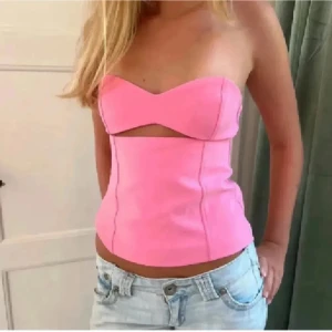 Rosa axelbandslös korsettopp - Trendig rosa korsettopp med axelbandslös bandeau-design och en snygg cut-out detalj framtill. Toppen har en figurnära passform och är perfekt att styla med jeans eller kjol för en cool look.