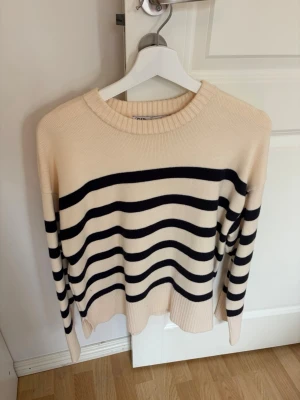 Randig stickad tröja från ZARA - Snygg stickad tröja från ZARA i beige med svarta horisontella ränder. Tröjan har rund halsringning, långa ärmar och ribbade muddar. Perfekt för en chill och trendig look.