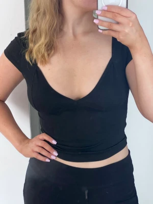 Svart croppad topp med v-ringning, nyskick - Croppad topp med djup v-ringning och figurnära passform. Så snygg att styla till jeans eller kjol!! Kan stylas y2k eller clean. Mjuk och stretchig.