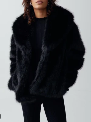 Svart fuskpälsjacka - Snygg svart fuskpälsjacka med bred krage och avslappnad passform. Jackan har en lyxig känsla och är perfekt för att hålla värmen under kalla dagar. Enkel att matcha med olika outfits och ger en trendig look.