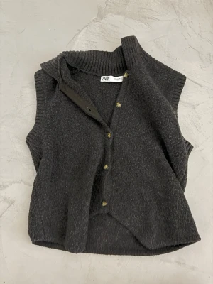 Mörkgrå stickad väst från Zara - Mysig mörkgrå stickad väst från Zara med ribbad krage och knappar framtill.