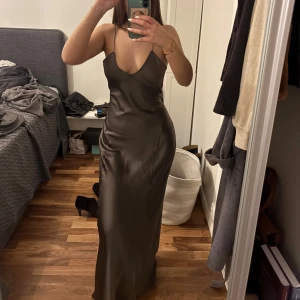 Mörkbrun långklänning i satin - mörkbrun/grå långklänning i satin med smala axelband och öppen rygg. Storlek M ❣️