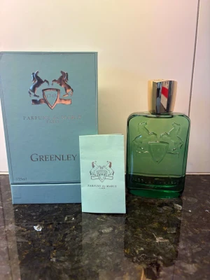 Parfums de Marly Greenley 125ml - Greenley från Parfums de Marly är en exklusiv parfym i en elegant grön glasflaska med silverfärgad kork. Flaskan har ett stilrent emblem med två hästar och levereras i en matchande ljusgrön kartong. Volymen är 125 ml och designen känns både lyxig och modern. Ca 123ML kvar!!