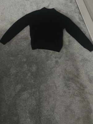 Svart stickad tröja - En enkel svart stickad tröja med rund hals som går upp lite och långa ärmar. Perfekt basplagg att matcha med olika outfits. Tröjan har en klassisk rak passform och är mjuk och bekväm.