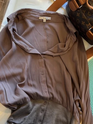 Brun långärmad blus från Oneness - Säljer en brun blus från Oneness med knappar framtill och bred ribbad mudd nedtill. Blusen har en lös passform och en bred krage som ger en avslappnad look. Materialet är mjukt och tunt, perfekt för att skapa en chill stil.