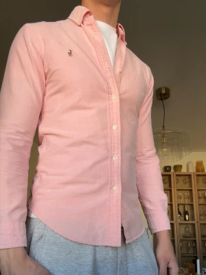 Rosa skjorta från Ralph Lauren - Snygg ljusrosa skjorta från Ralph Lauren med klassisk krage och knäppning framtill. Väldigt fint skick!