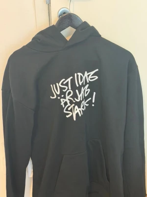 Hammarby tröja - Svart Hammarby hoodie med huva och vit graffiti-inspirerad text på bröstet som säger 'Just idag är jag stark!'. Hoodien har en klassisk passform och en stor magficka framtill. Perfekt för en avslappnad och cool stil. 