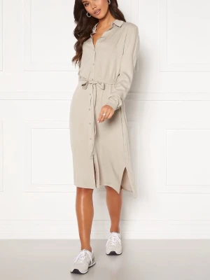 Beige skjortklänning med knytband - Stilren beige skjortklänning med knappar framtill och knytband i midjan. Klänningen har lång ärm, krage och slitsar i sidorna för en avslappnad look. Perfekt för dig som gillar enkel och clean stil.
