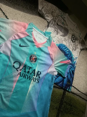 PSG x BRAZIL - Säljer en Paris Saint-Germain matchtröja från Nike i unika pastellfärger med turkos, rosa och lila nyanser. Tröjan har PSG-logga, Qatar Airways-tryck och sportig design med korta ärmar. Perfekt för fotboll eller streetwear.