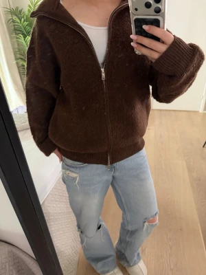 Brun fluffig ziptröja från Zara - Mysig brun ziptröja från Zara med fluffig textur och ribbade muddar. Tröjan har hög krage och dragkedja hela vägen. Perfekt för lager-på-lager och chill dagar.
