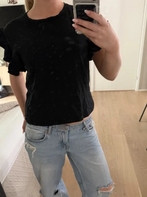 Svart volangtopp från Zara - Svart topp från Zara med volangdetaljer på ärmarna. T-shirten har rund halsringning och är tillverkad i mjuk bomull. Perfekt för en chill och stilren look.
