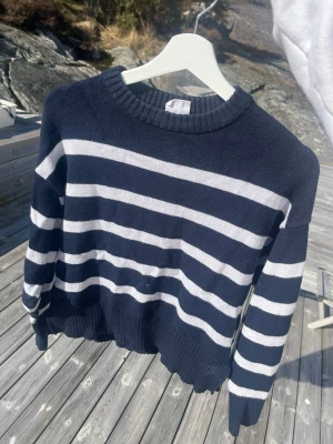 Marinblå randig stickad tröja - Stickad tröja i marinblått med vita horisontella ränder. Tröjan har rund halsringning, långa ärmar och ribbstickade muddar vid ärmslut och nederkant. Perfekt för en avslappnad och stilren look.
