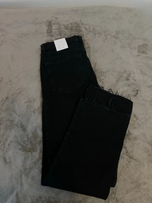 Svarta crop flare jeans från Zara - Säljer ett par svarta crop flare jeans från Zara med råa, fransiga benslut. Jeansen har klassisk femficksdesign och är tillverkade i ett stretchigt material som sitter snyggt. Perfekta för dig som gillar trendiga och bekväma jeans.