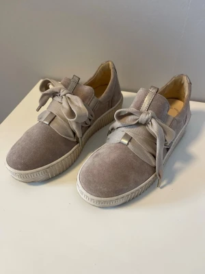 Beige/ljusrosa/ljusgrå sneakers från Gabor med breda snören - Snygga beige sneakers från Gabor med breda, matchande snören och en robust sula. Skorna är tillverkade i mocka och har en låg profil som ger en stilren look. Perfekta för dig som vill ha både komfort och trendig design. Dom är också impregnerade och redo att använda. Nypris: 1350kr.