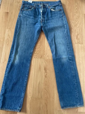 Levi's 501 32/32 - Klassiska blå jeans från Levi's med rak passform och fem fickor. Jeansen har en knappgylf och tydliga sömmar, samt den ikoniska läderlappen bak i midjan. Tillverkade i slitstark denim som ger en tidlös look.