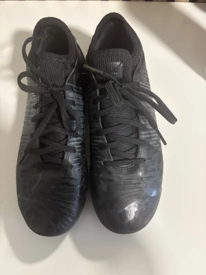 Svarta fotbollsskor från Puma - Säljer ett par inomhus helsvarta fotbollsskor från Puma med snörning och låg profil. Skorna har en mönstrad ovansida och sula för bra grepp på innne planen. Tillverkade i syntetmaterial och designade för att ge bra bollkontroll och komfort under spelet. (De finns även knäskydd som man får gratis, men det är använda) nypris 1200kr!